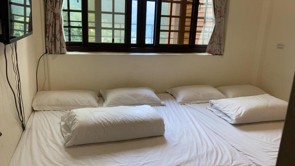 a bed with four pillows in a room with a window at 金蘭小築民宿 in Zhuqi