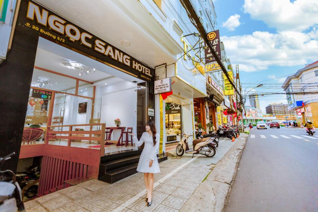 Uma mulher de vestido branco a andar numa rua da cidade. em Ngọc Sang 1 Hotel em Da Lat