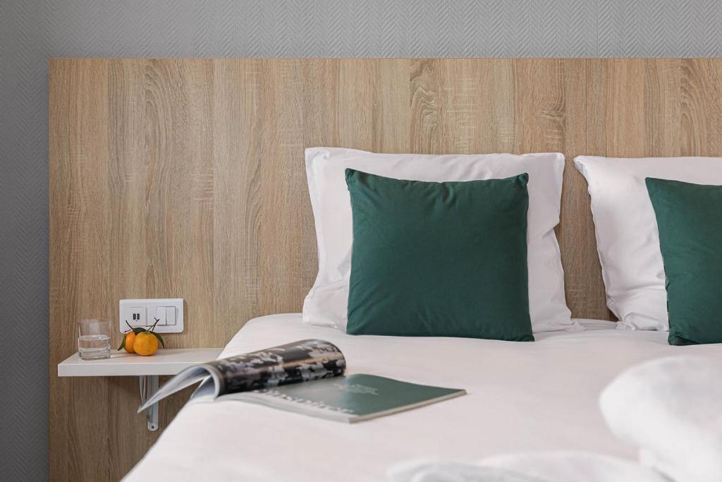 Una cama con almohadas verdes y un libro. en Hotel L'Abri en Le Puy-en-Velay