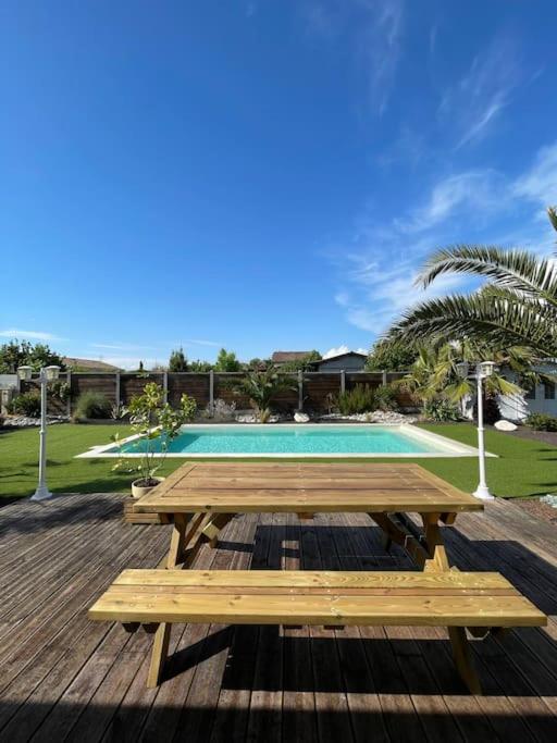 une terrasse en bois avec une table de pique-nique et une piscine dans l'établissement Charmante Maison entre châteaux et océan, à Cussac-Fort-Medoc