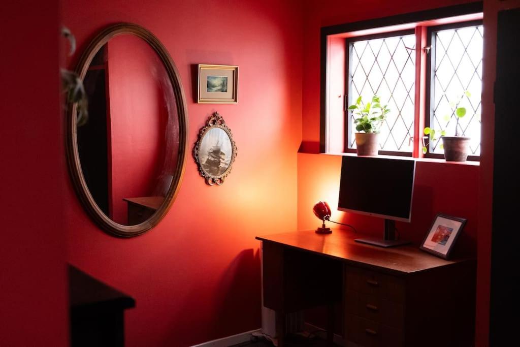 a red room with a desk with a computer and a mirror at Charming apartment in central Stavanger in Stavanger