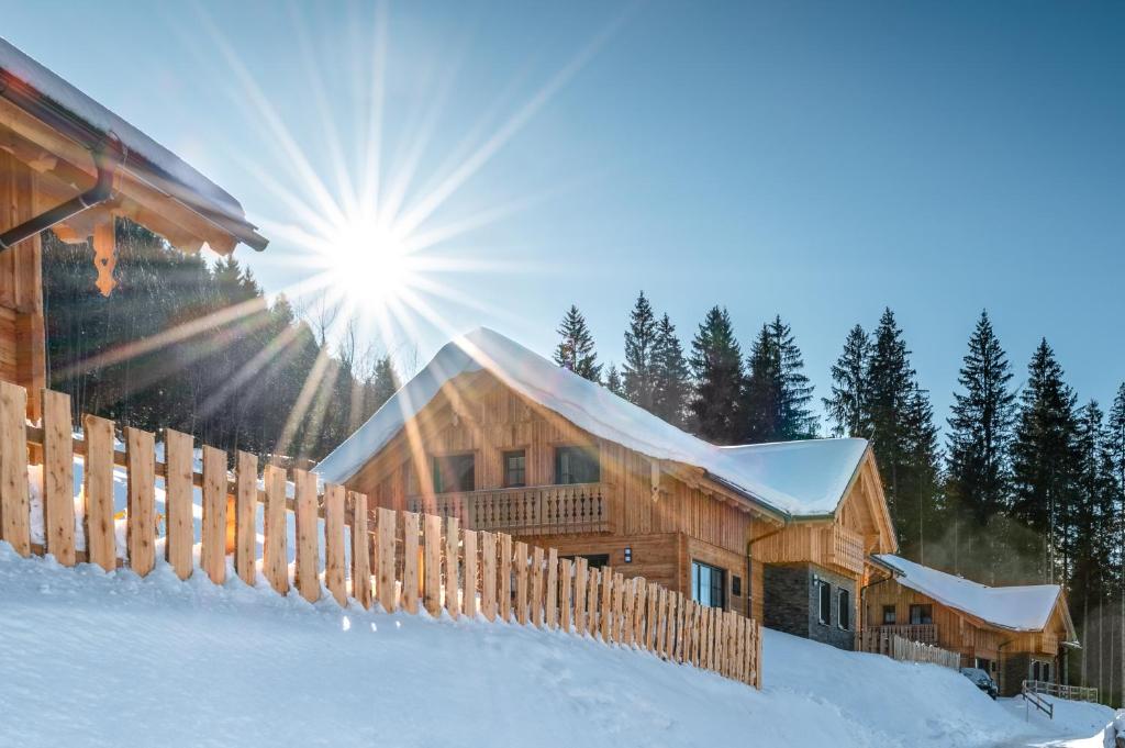 a log cabin in the snow with the sun behind it at Poolchalet Dachsteinblick in Pruggern