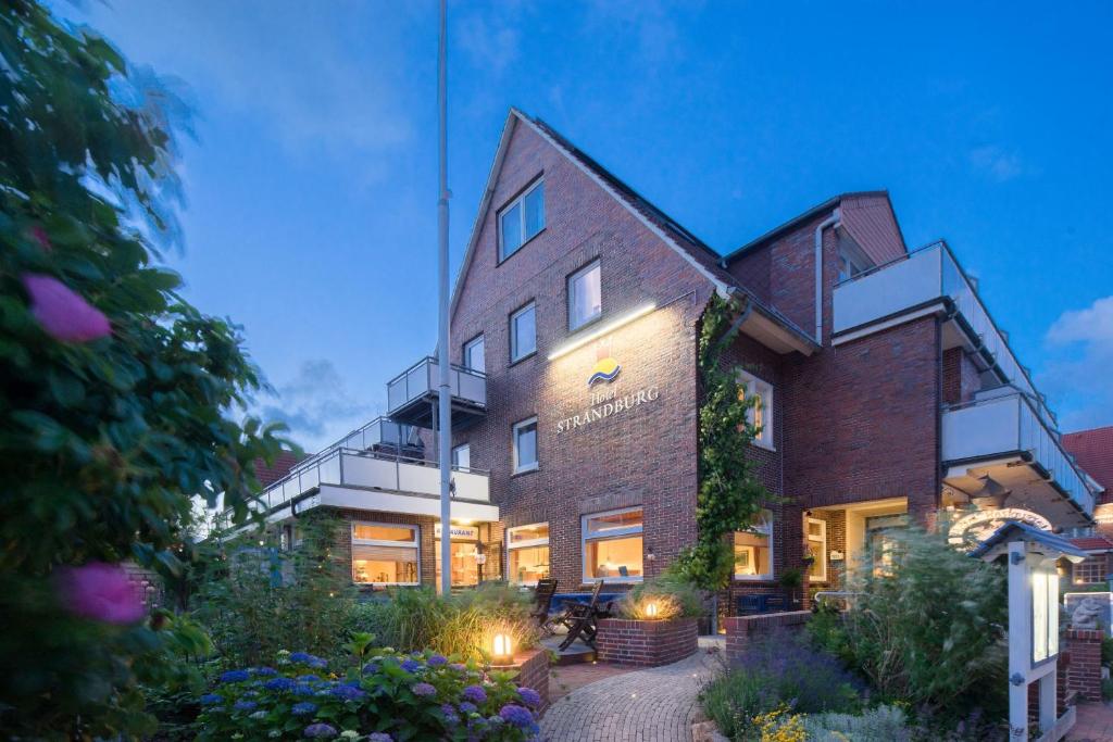 Un grand bâtiment en briques avec des lumières allumées dans l'établissement Hotel Strandburg, à Baltrum