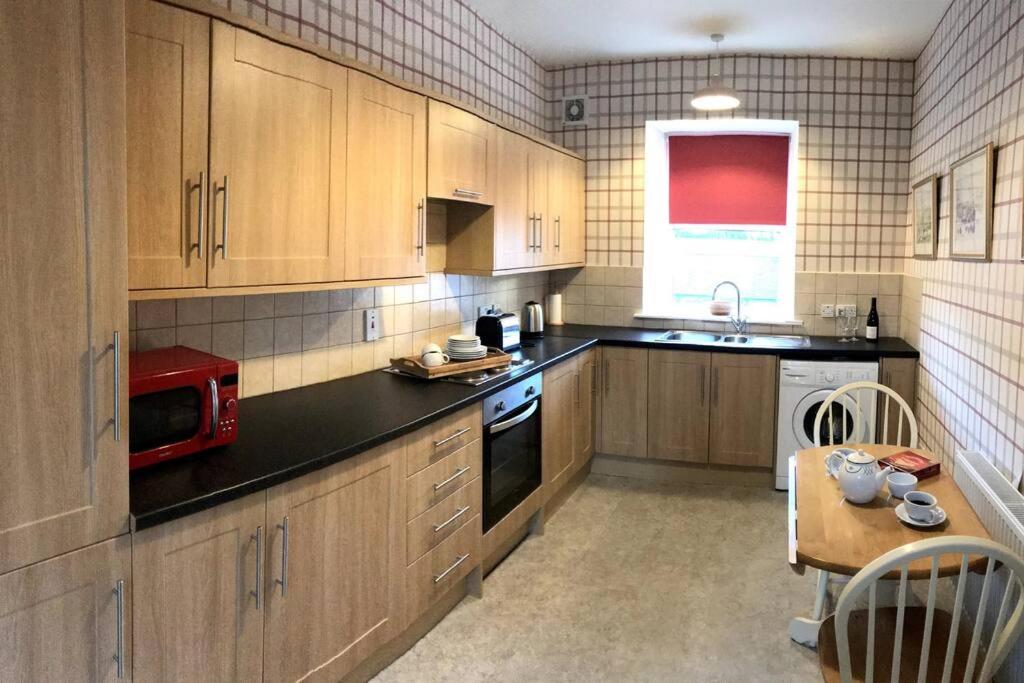 a kitchen with wooden cabinets and a table with a microwave at Cosy Wee Cottage St Andrews 20 in Ceres
