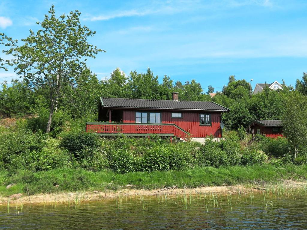 ein rotes Haus auf einem Hügel neben einem Wasserkörper in der Unterkunft Holiday Home Staksholmen - SOW725 by Interhome in Konsmo