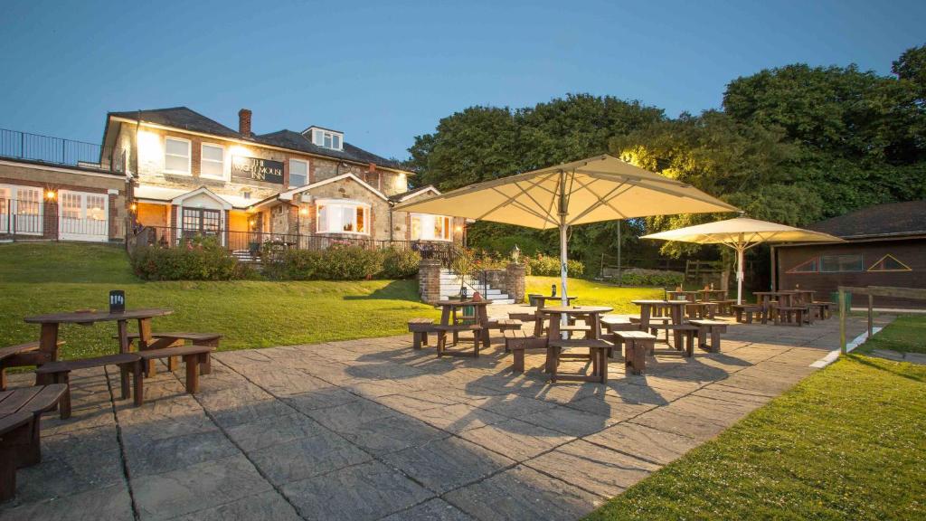 The Wight Mouse Inn في Chale: مجموعة من طاولات التنزه والمظلات أمام المنزل