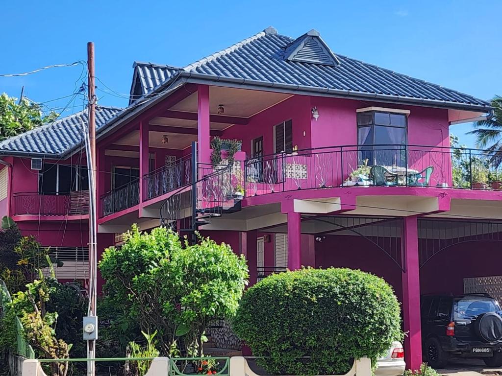 a pink house with a balcony and bushes at The Seaside Garden Guesthouse in Buccoo