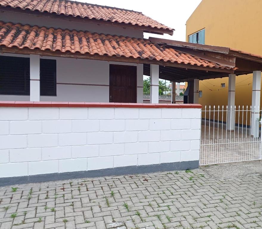 une maison avec un mur blanc et une clôture dans l'établissement Casa na praia do Sonho, à Palhoça