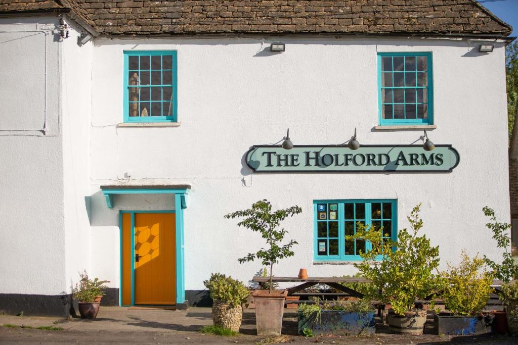 een wit gebouw met een bord dat de tuinwapens leest bij The Holford Arms in Tetbury