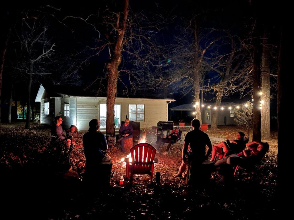 a group of people sitting around a fire at night at Owl Hoot Lake Retreat- Dock, beach & wooded haven! in Texanna