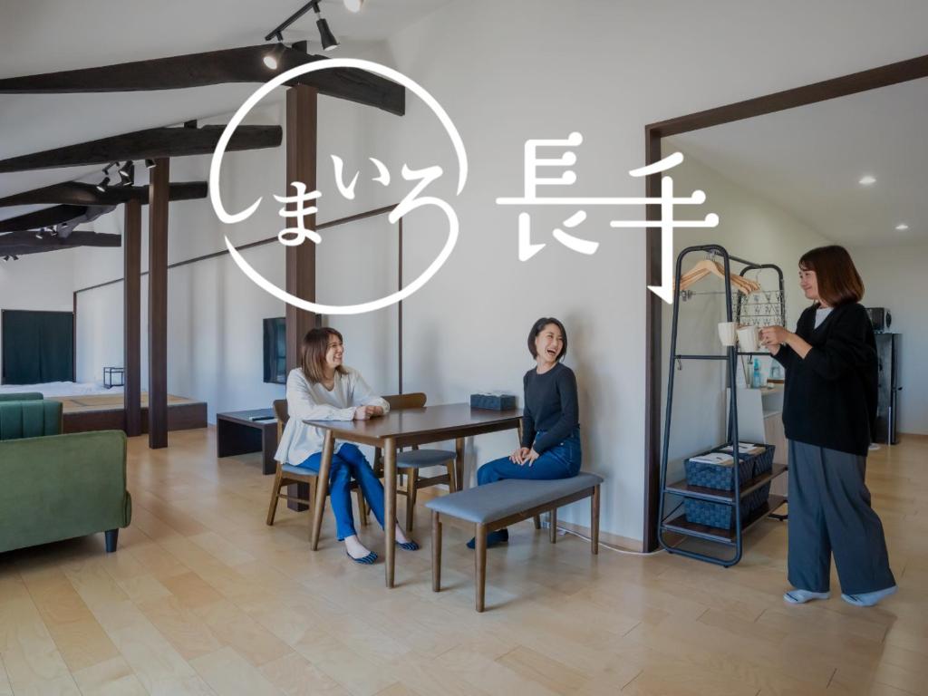 two women sitting at a table in a room at 丘の上から海が見える一棟貸しヴィラ しまいろ長手 