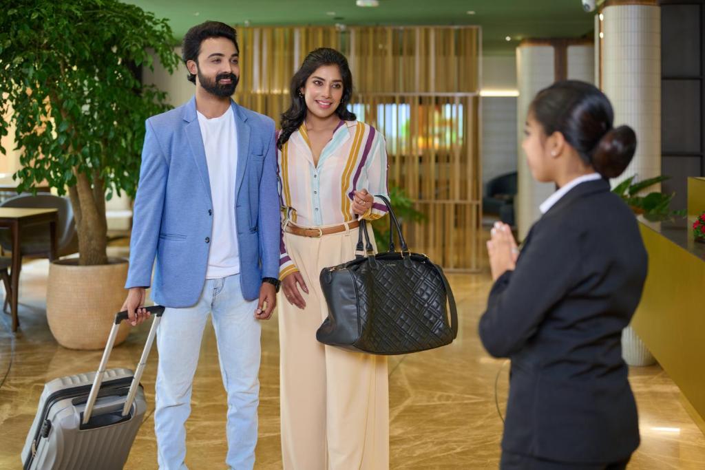a man and woman standing next to a woman with a suitcase at Flora Airport Hotel and Convention Centre Kochi in Nedumbassery