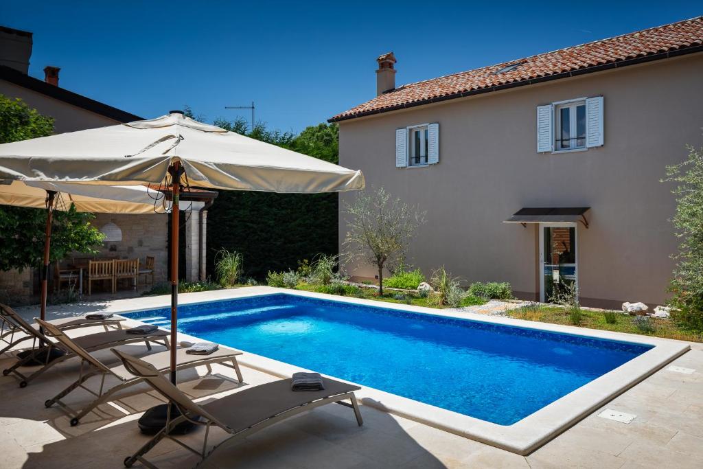ein Pool mit zwei Stühlen und einem Sonnenschirm neben einem Haus in der Unterkunft Villa Vin - Pool, ruhig, strandnah, Klimaanlage, Außenküche, Meeresnähe, Gästebetreuer in Babići