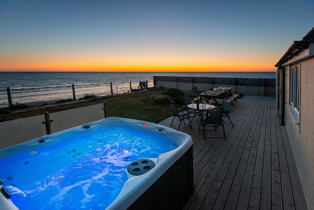 a jacuzzi tub on a deck with a view of the ocean at Sound of the Sea, beach front Bungalow with hot tub, in Tywyn in Tywyn