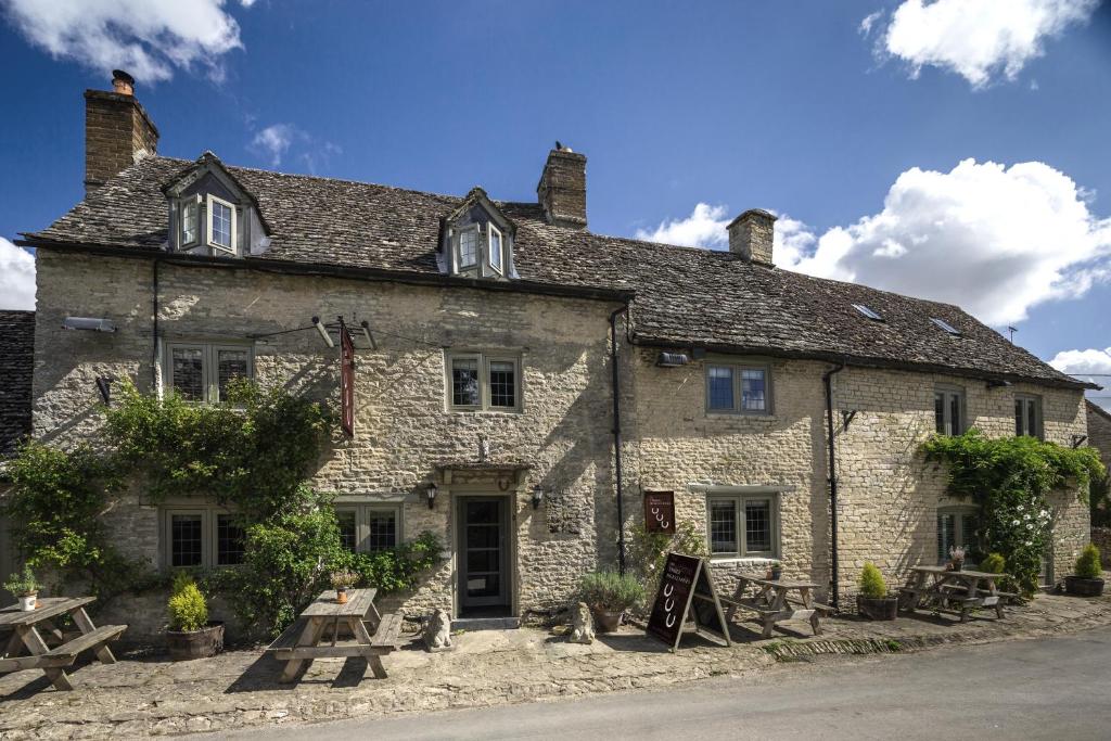 um velho edifício de pedra com mesas de piquenique em frente em The Three Horseshoes em Burford