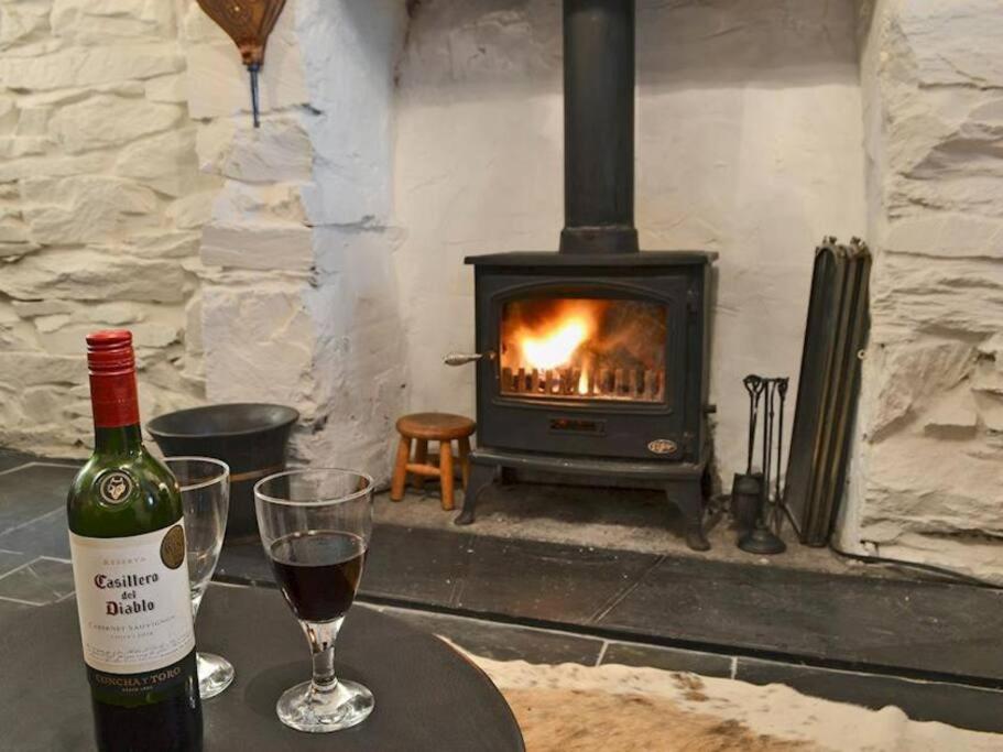 una botella de vino y copas en una mesa frente a la chimenea en Cosy terrace cottage built into the mountain side. en Blaenau-Ffestiniog