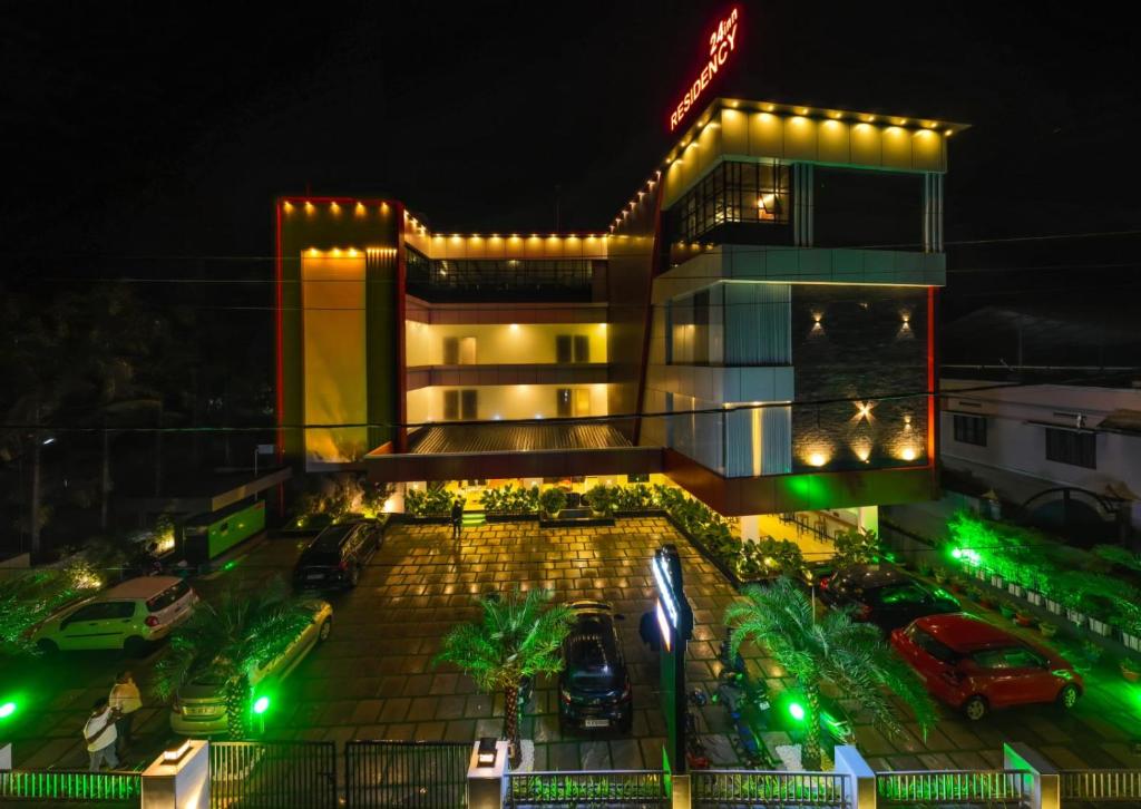 hotel 24inn residency في Pathanāmthitta: مبنى فيه سيارات تقف في موقف السيارات في الليل
