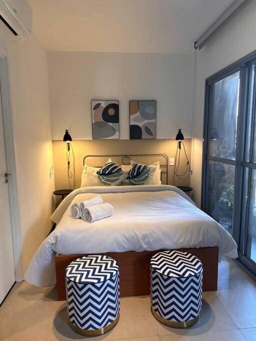 a bedroom with a large bed with two ottomans at Estúdio VN Consolação in Sao Paulo