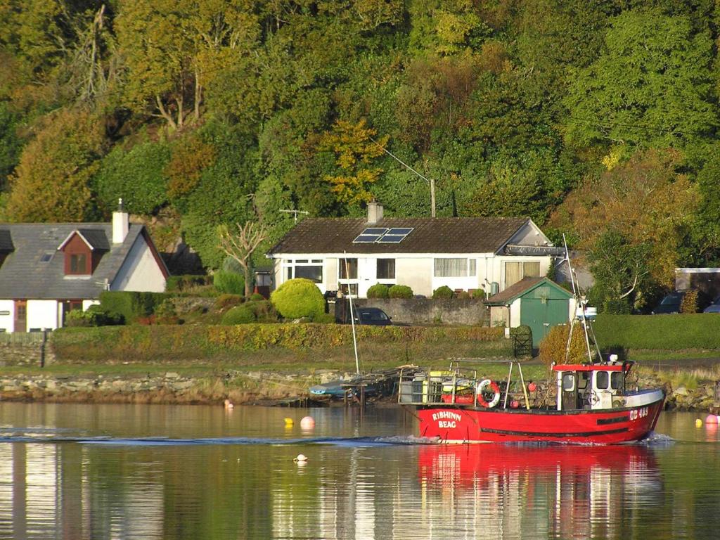 2 bed in Lochgilphead AG692 في Tayvallich: قارب احمر في الماء بالقرب من منزل