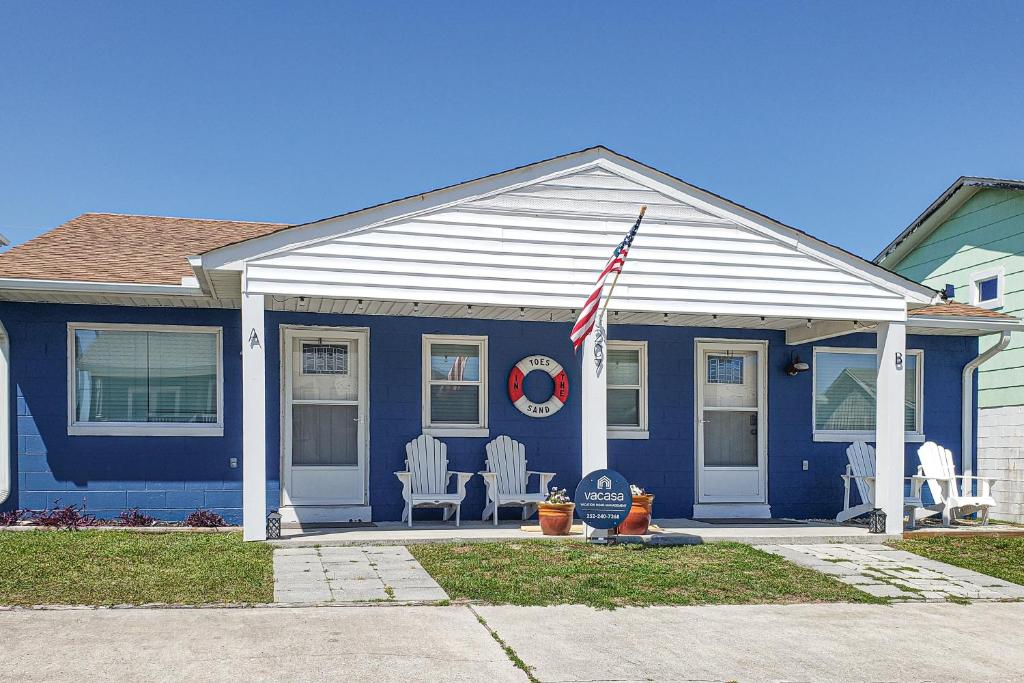 ein blaues Haus mit zwei weißen Stühlen und einer amerikanischen Flagge in der Unterkunft Toes In The Sand in Atlantic Beach