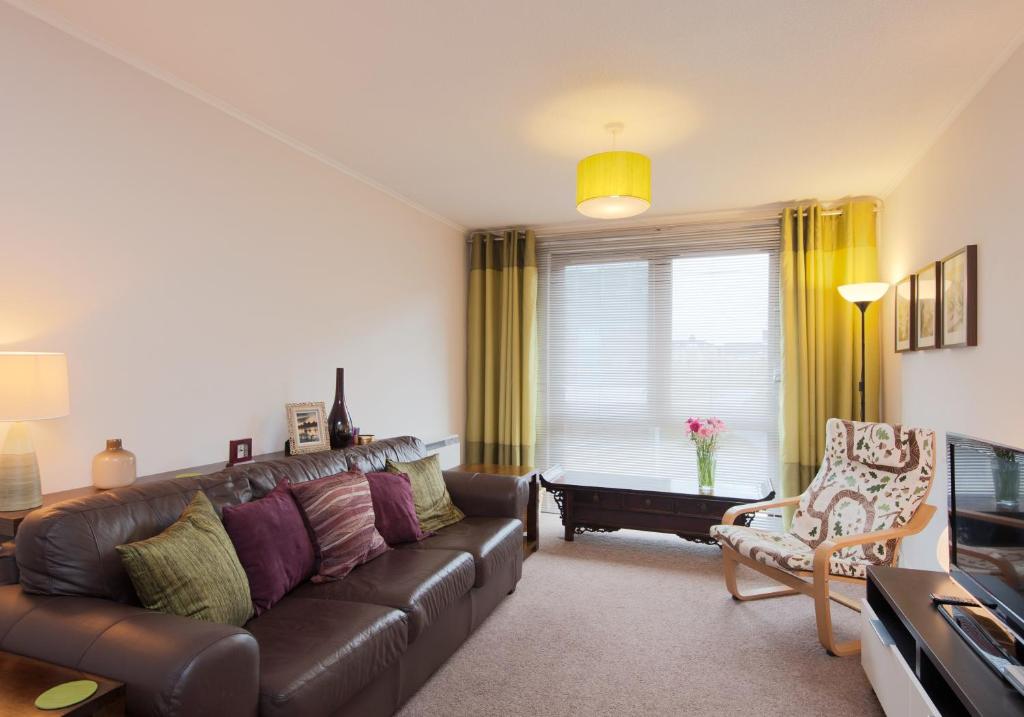 sala de estar con sofá de cuero marrón y silla en Logie Green Road Apartment, en Edimburgo