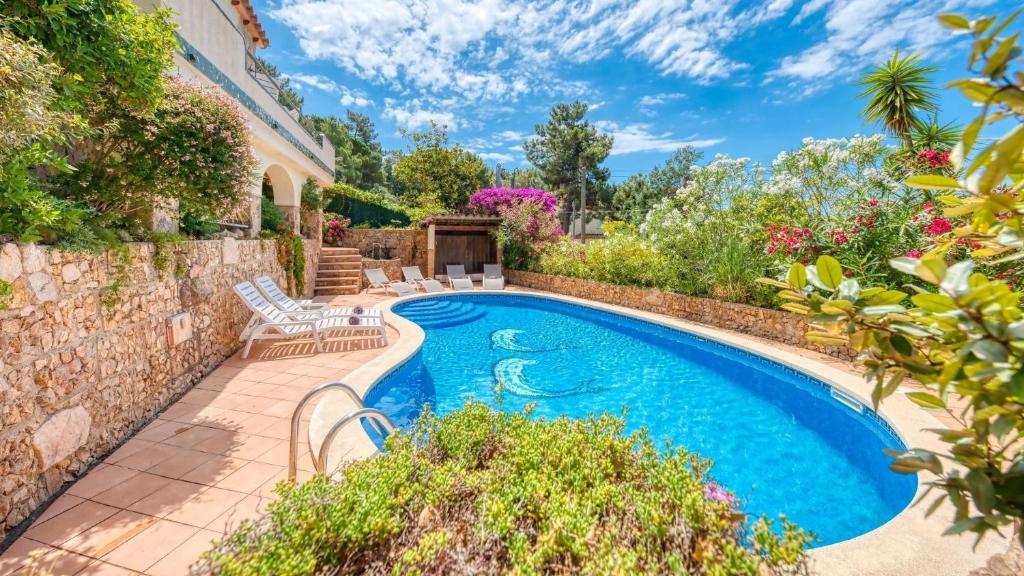 einen Pool in einem Garten mit einer Steinmauer in der Unterkunft Costacabana - Villa Cleo in Lloret de Mar