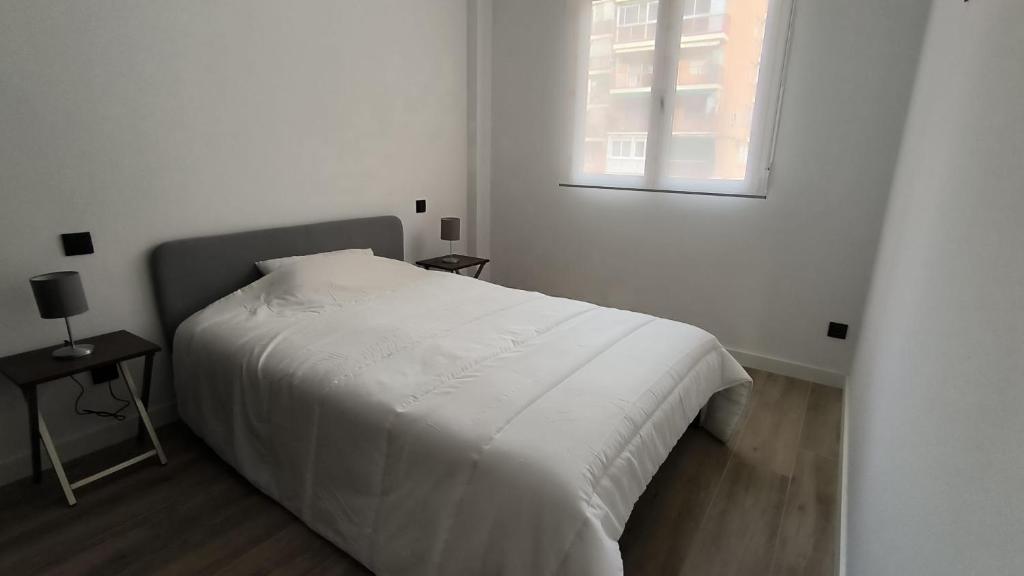 a white bedroom with a bed and a window at Exyca Metropolitano in Madrid