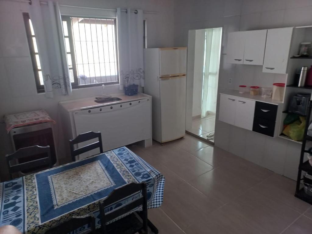 een keuken met witte kasten, een tafel en een koelkast bij Casa de Praia Mongaguá in Mongaguá