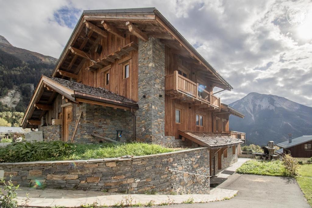 a wooden house with a balcony on a stone wall at Chalet Alpin Luxe, Jacuzzi, Vue in Champagny-en-Vanoise