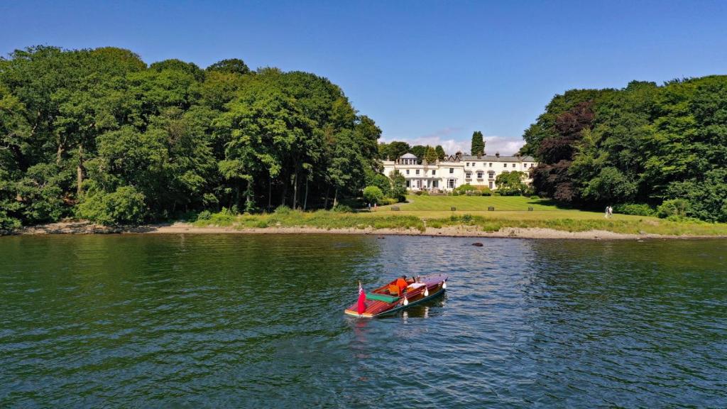 a boat in the water in front of a house at Storrs Hall Hotel in Bowness-on-Windermere