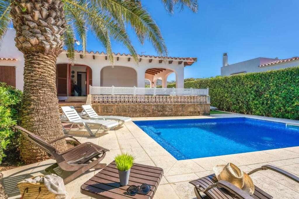 a villa with a swimming pool and a palm tree at Aure Villa con piscina y aire acondicionado! in Cala'n Bosch