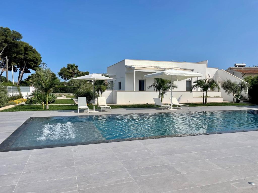 a swimming pool with chairs and umbrellas in front of a house at LM7 Luxury Villa Sicily in Fontane Bianche