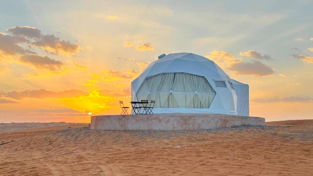 a tent in the desert with the sunset in the background at Starry Domes Desert Camp II in Badīyah