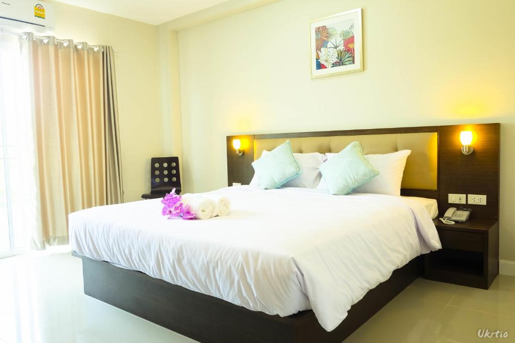 A large bed sits against a lit dark wood headboard beside a curtained window.