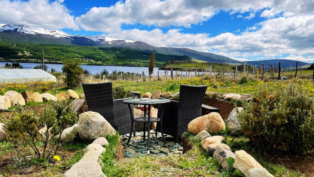una mesa y sillas en un campo con un lago y montañas en Cabaña - Granja Lago Frío en Coihaique