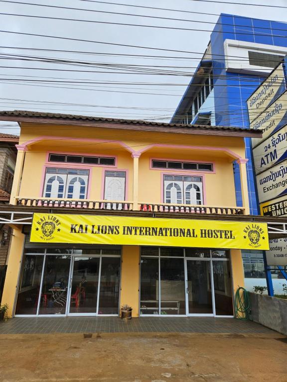 un bâtiment jaune avec un panneau devant lui dans l'établissement Kai Lions International Hostel, à Muang Pakxong