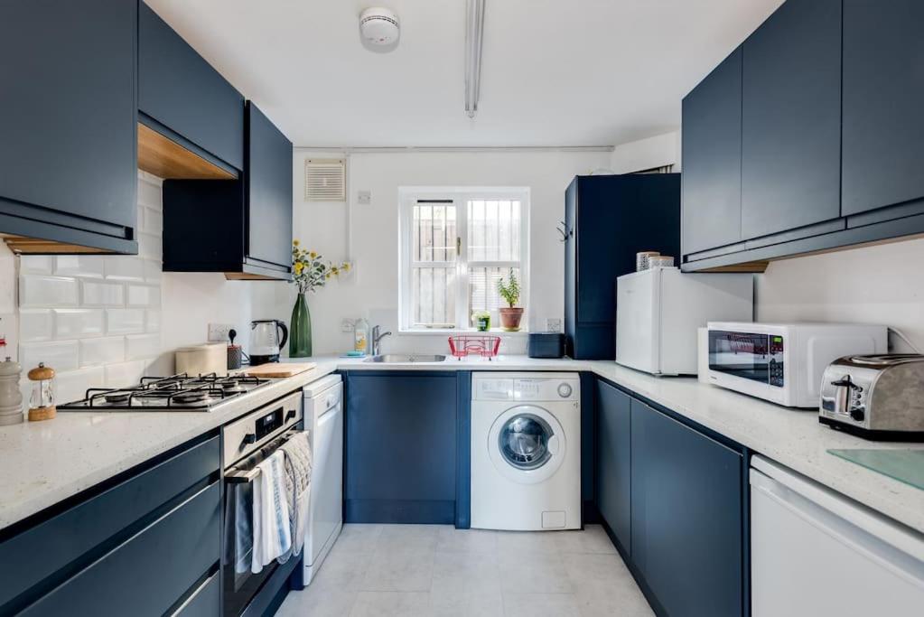 a kitchen with blue cabinets and a washing machine at Cosy 2-Bedroom Haven in Picturesque Headington in Oxford