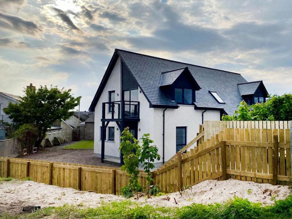 a white house with a black roof and a wooden fence at On The Beach-uk7465 in Balintore