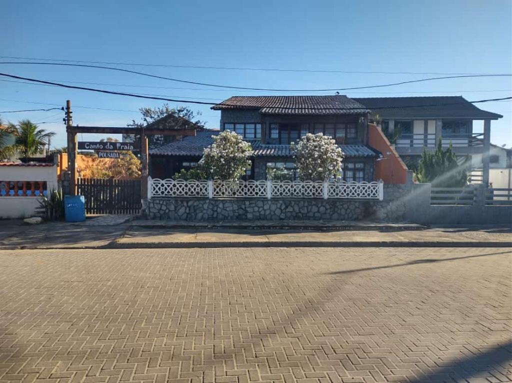 a house with a white fence in front of a street at Pousada Canto da Praia in São Pedro da Aldeia