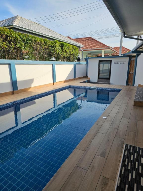 a swimming pool with a wooden deck and a house at Pool Villa Baan Sanook Cha-am in Cha Am