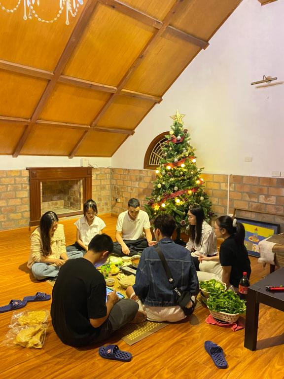 eine Gruppe von Menschen, die um einen Weihnachtsbaum herum auf dem Boden sitzen in der Unterkunft GÁC home & decor in Hanoi