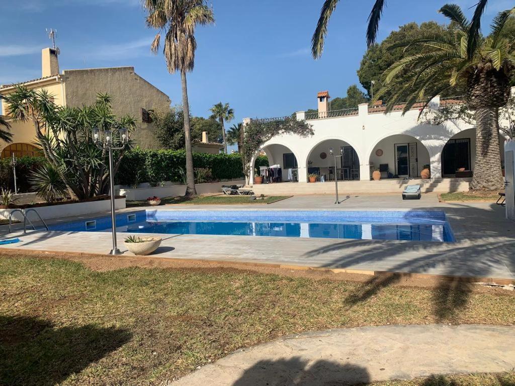 a swimming pool in front of a house with palm trees at VILLA LOS TRES SOLES in Les tres Cales