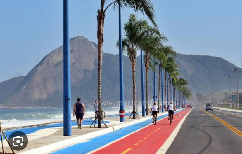 a group of people riding bikes down a sidewalk with palm trees at Kitnet dos Alves in Maricá