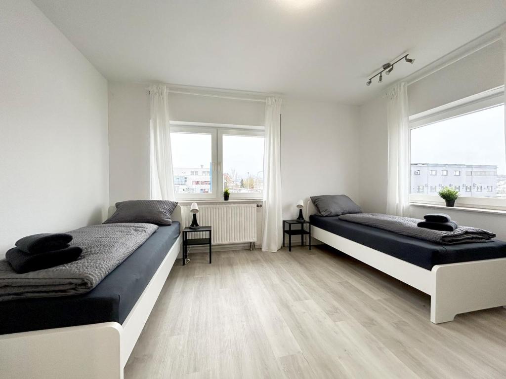 two beds in a white room with two windows at Cozy Apartment in Eichenzell