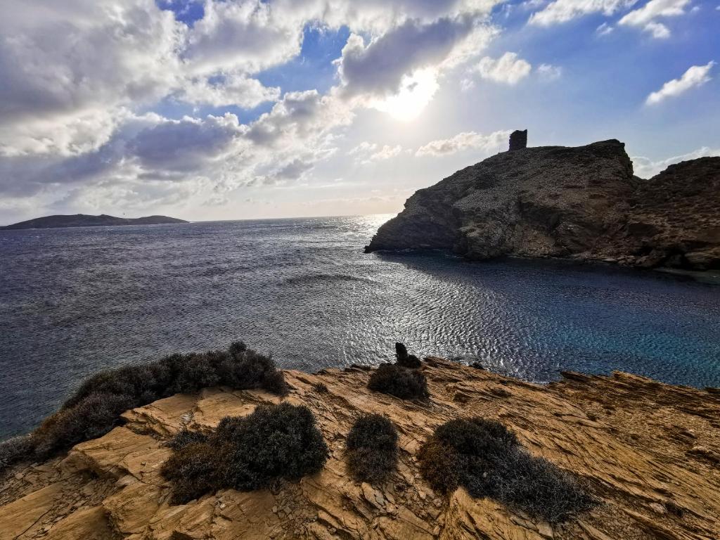 une personne assise sur une falaise près de l'eau dans l'établissement Andros Country Residence, à Makrotándalon