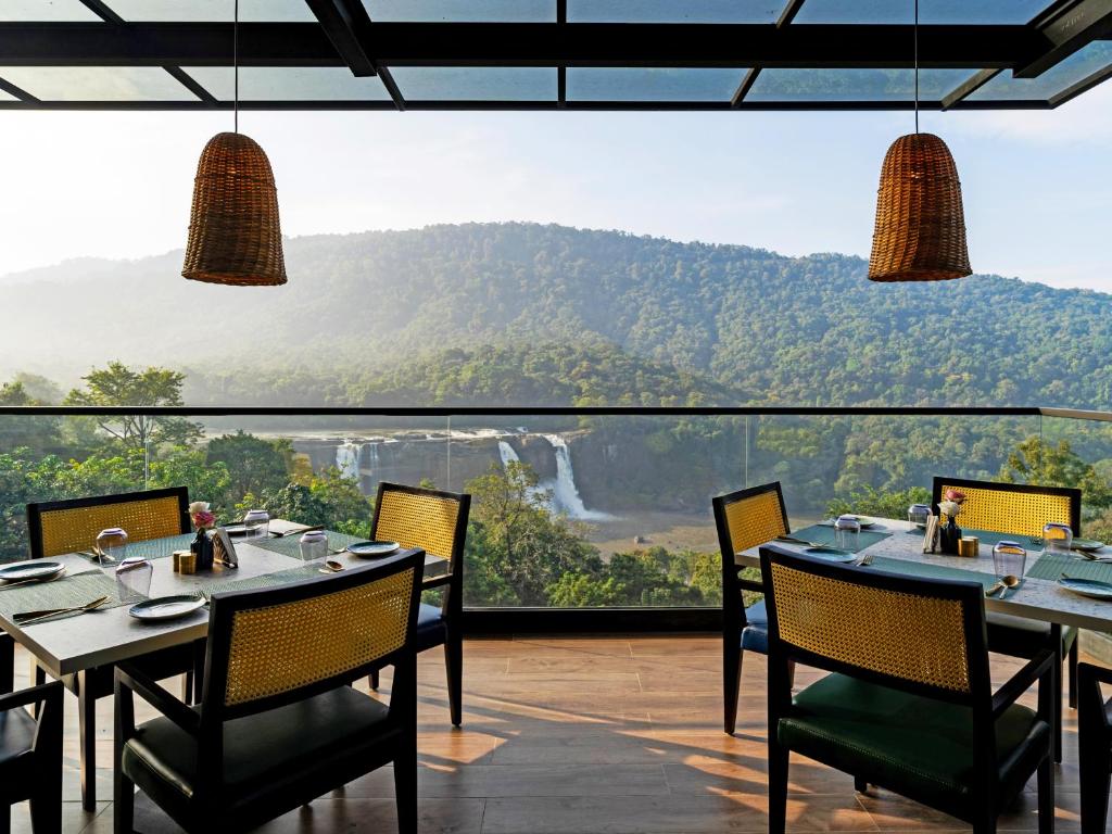 a restaurant with tables and chairs and a view of a waterfall at Flora Misty Falls Athirappilly in Athirappilly