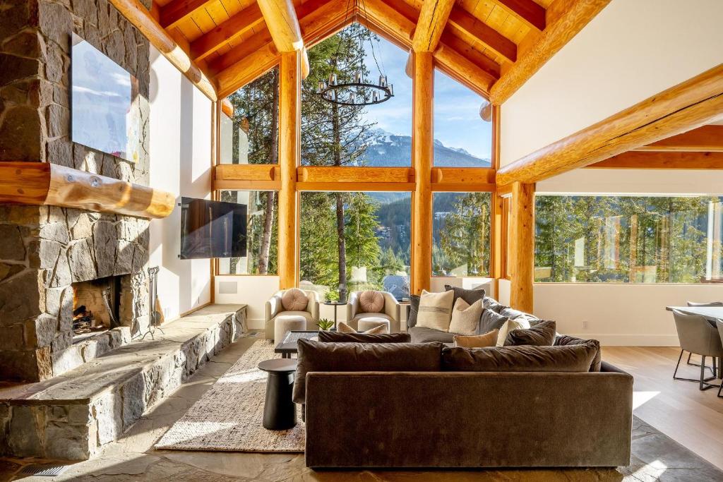 een woonkamer met een stenen open haard en een groot raam bij Peak2Peak Chalet - Stunning Log Chalet w/ Mountain Views & Hot Tub - Whistler Platinum in Whistler