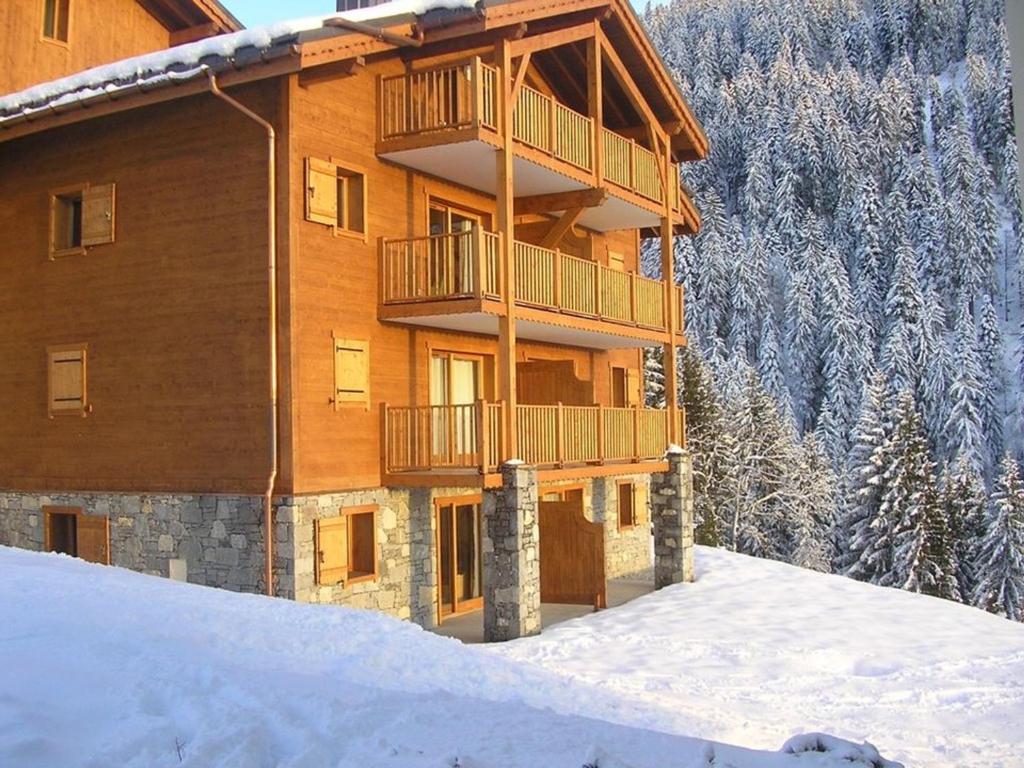 un grand bâtiment en bois avec un balcon dans la neige dans l'établissement Appartement avec Terrasse, Jardin et Piscine Chauffée à Crest-Voland - 6 Pers. - FR-1-733-136, à Crest-Voland