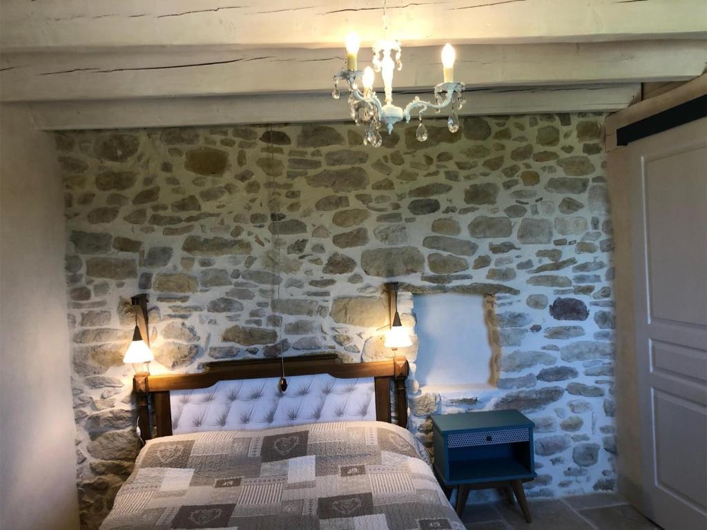 um quarto com uma parede de pedra, uma cama e um lustre em Gîte Figuier au Mas Dujau em Saint-Sauveur-de-Cruzières