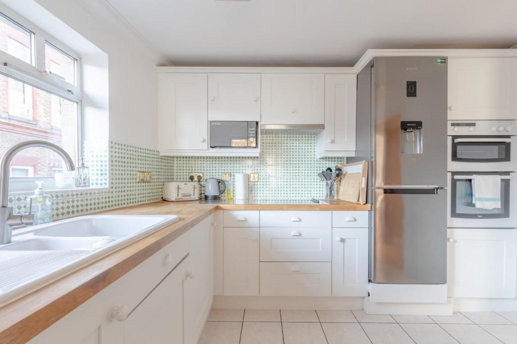 a kitchen with white cabinets and a stainless steel refrigerator at Spacious 3BD Flat - 14 Mins to Buckingham Palace! in London